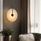 Black-arm Clérachic Plug-In Wall Sconce on charcoal, warm disc above a fern and a dark armchair with a shaggy white pillow.