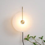 Clérachic Plug-In Wall Sconce lit on an off-white wall, gold arm and black cord beside thin, thorny plant branches.