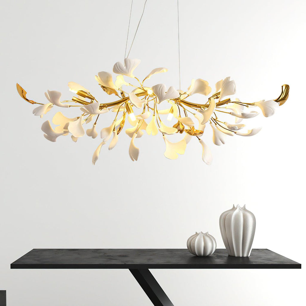Clérachic chandelier seen close, its gold curving branches and white leaves lit, above a black console holding two white ribbed vases.