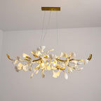 Clérachic leaf chandelier lit against a plain light wall, its gold curved branch ends rising either side of the white porcelain leaves.