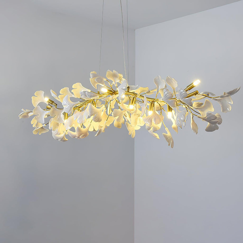 Lit Clérachic chandelier of white ginkgo leaves and small candle-style bulbs, hung in a room corner with pale grey walls.