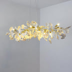 Lit Clérachic chandelier of white ginkgo leaves and small candle-style bulbs, hung in a room corner with pale grey walls.