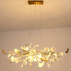 Clérachic chandelier glowing warm amber from a gold canopy, light spilling through the white leaves onto the peach ceiling.