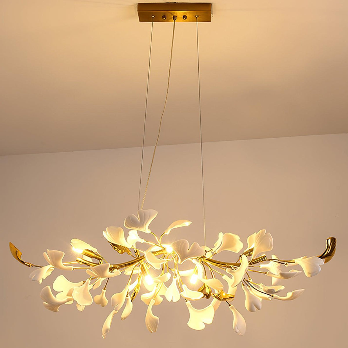 Clérachic chandelier glowing warm amber from a gold canopy, light spilling through the white leaves onto the peach ceiling.