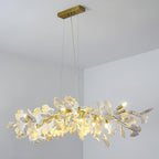 Clérachic leaf chandelier hanging from a gold canopy in a pale grey corner, bulbs on and white leaves lit from within.