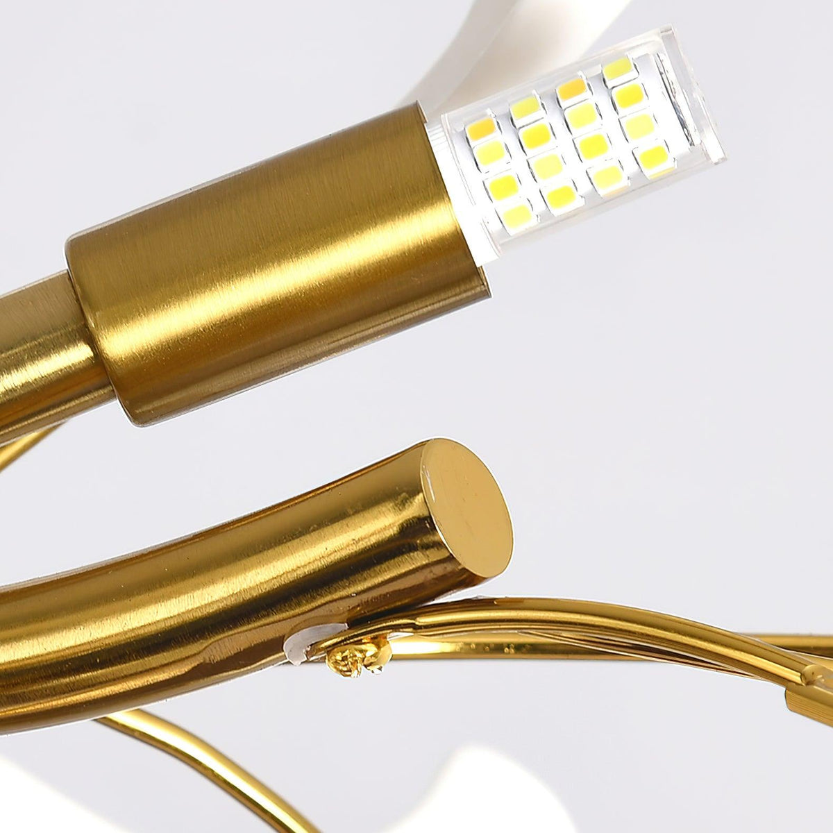 Close view of a gold lamp holder with a small LED capsule and a bare curved gold branch on this Clérachic chandelier.