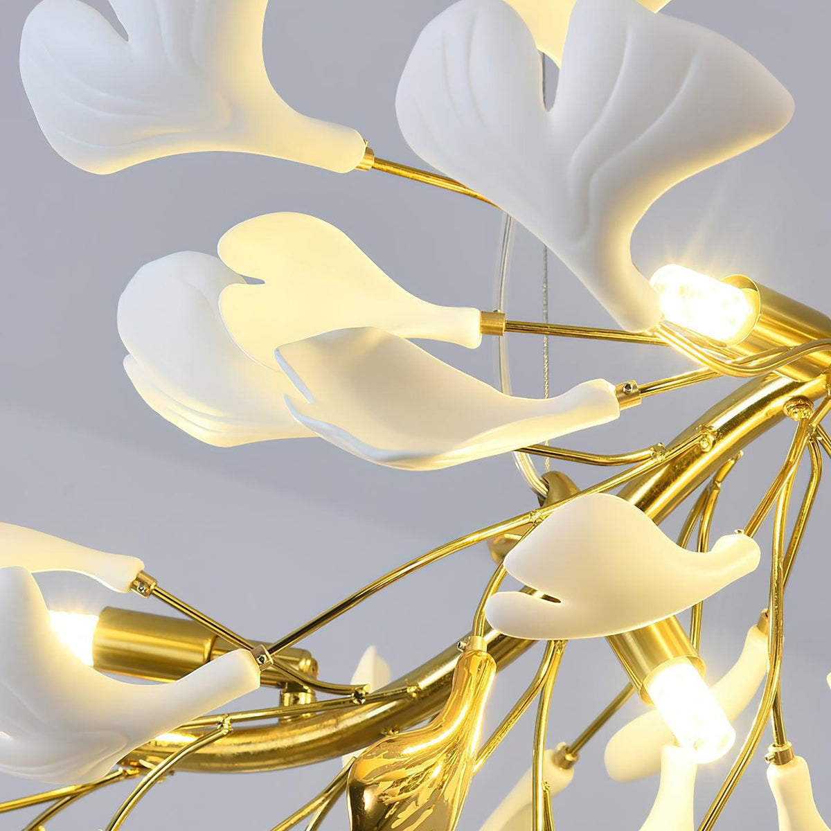 Close view of lit LED capsules in gold holders among white leaves on this Clérachic chandelier, thin hanging cable behind.