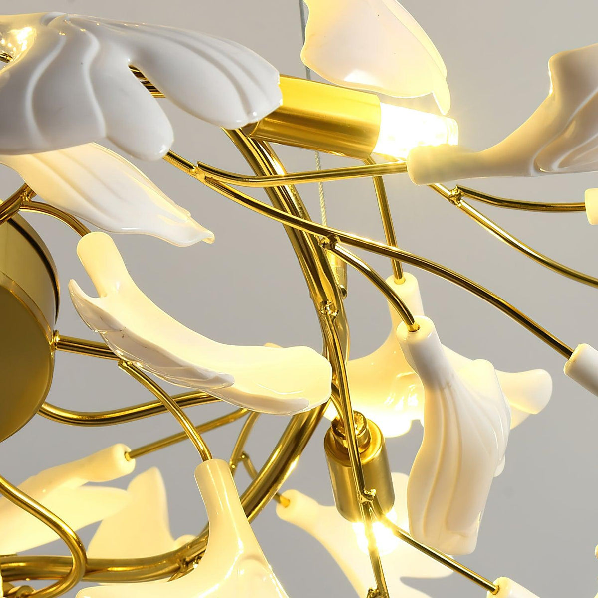 Detail of a lit bulb holder and the curved gold central frame of this Clérachic chandelier, white leaves wrapped around it.