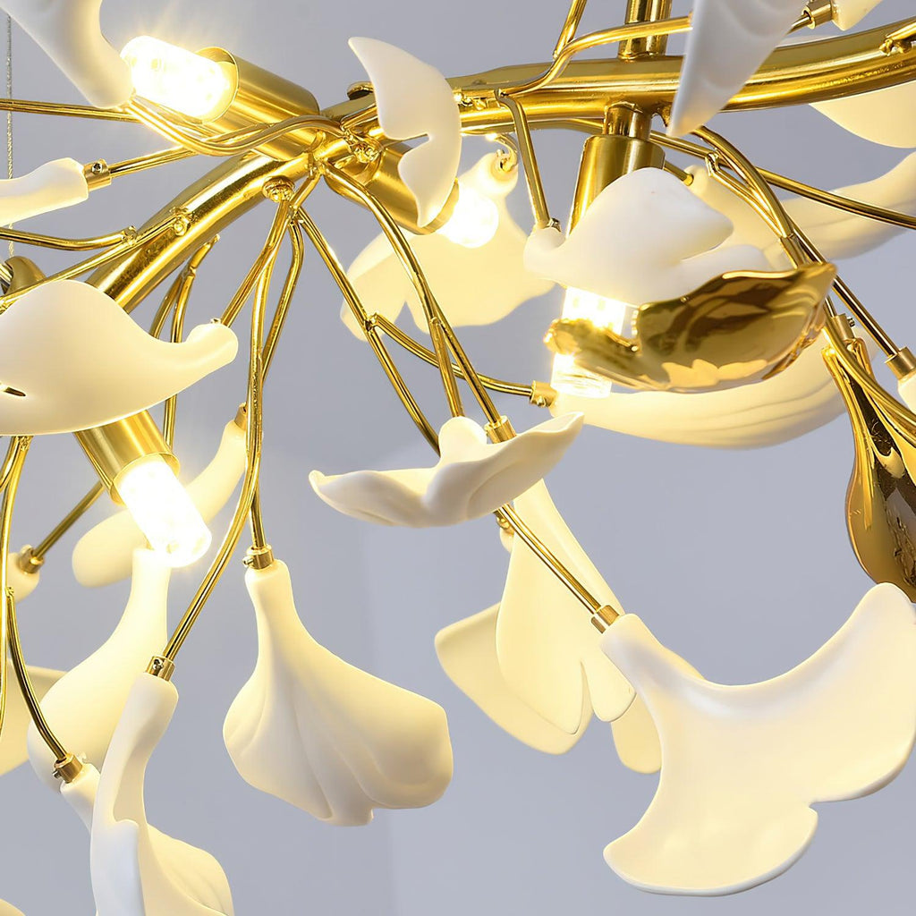 Close view from below of white ginkgo leaves glowing round lit bulbs on this Clérachic chandelier, with a gold leaf-shaped accent.
