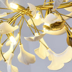 Close view from below of white ginkgo leaves glowing round lit bulbs on this Clérachic chandelier, with a gold leaf-shaped accent.