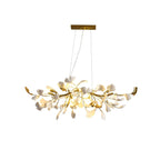 Lit Clérachic gold-bodied chandelier with white leaves and upturned gold tips, shown whole on a plain white backdrop.