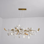 Clérachic chandelier with gold branches and white leaves, photographed from slightly below against a pale grey wall and ceiling.
