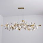 Unlit Clérachic chandelier with gold curved branches and white leaves, hanging from a gold canopy in a grey room corner.