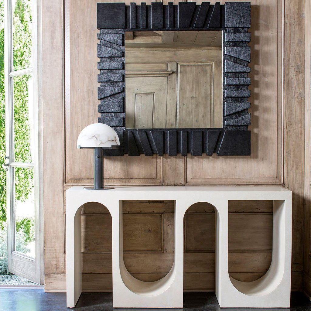 Small Clérachic table lamp with a dark base on a white arched console, below a mirror in a heavy black frame on a timber-panelled wall.
