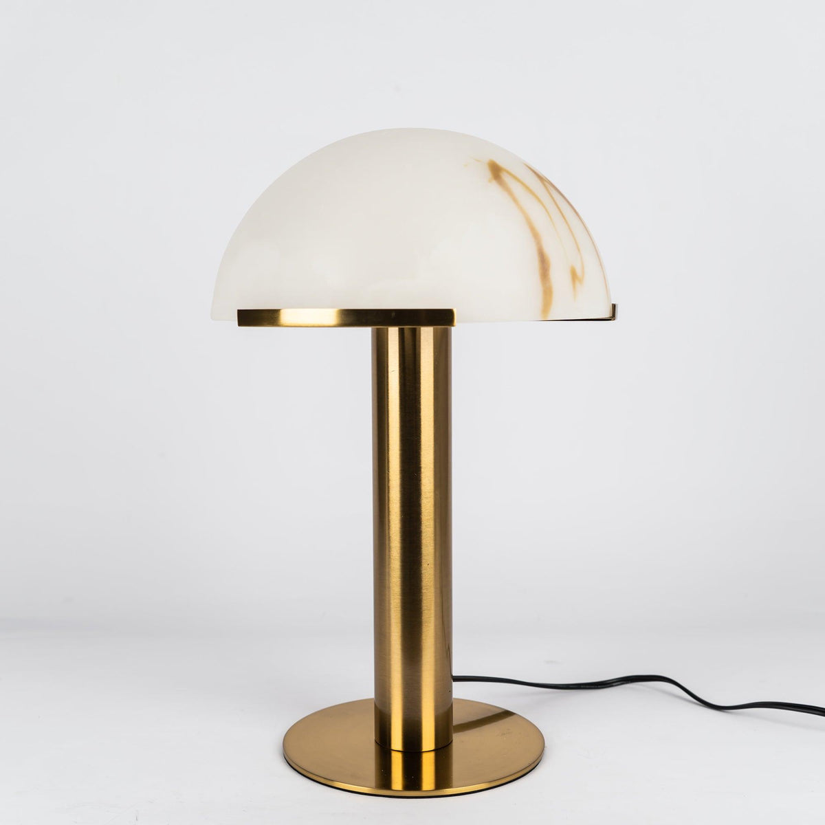 Unlit gold Clérachic table lamp against light grey, the alabaster dome showing honey-coloured streaks above a round brushed base.