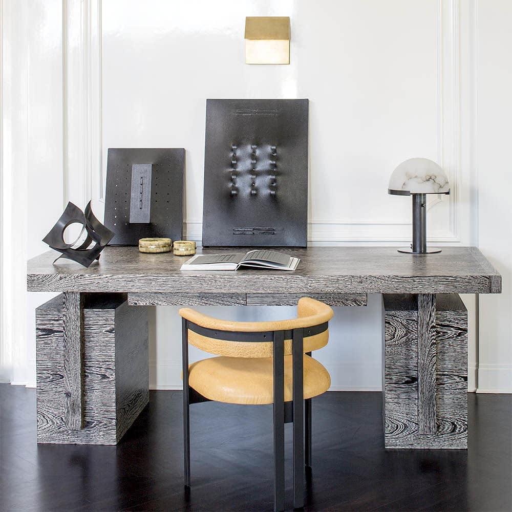 Dark-based Clérachic table lamp on a weathered grey oak desk, with framed black artworks and a tan leather chair in a white room.
