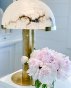 Close view of this Clérachic table lamp's dark-veined alabaster dome and brass stem, with a bunch of pale pink peonies in front.