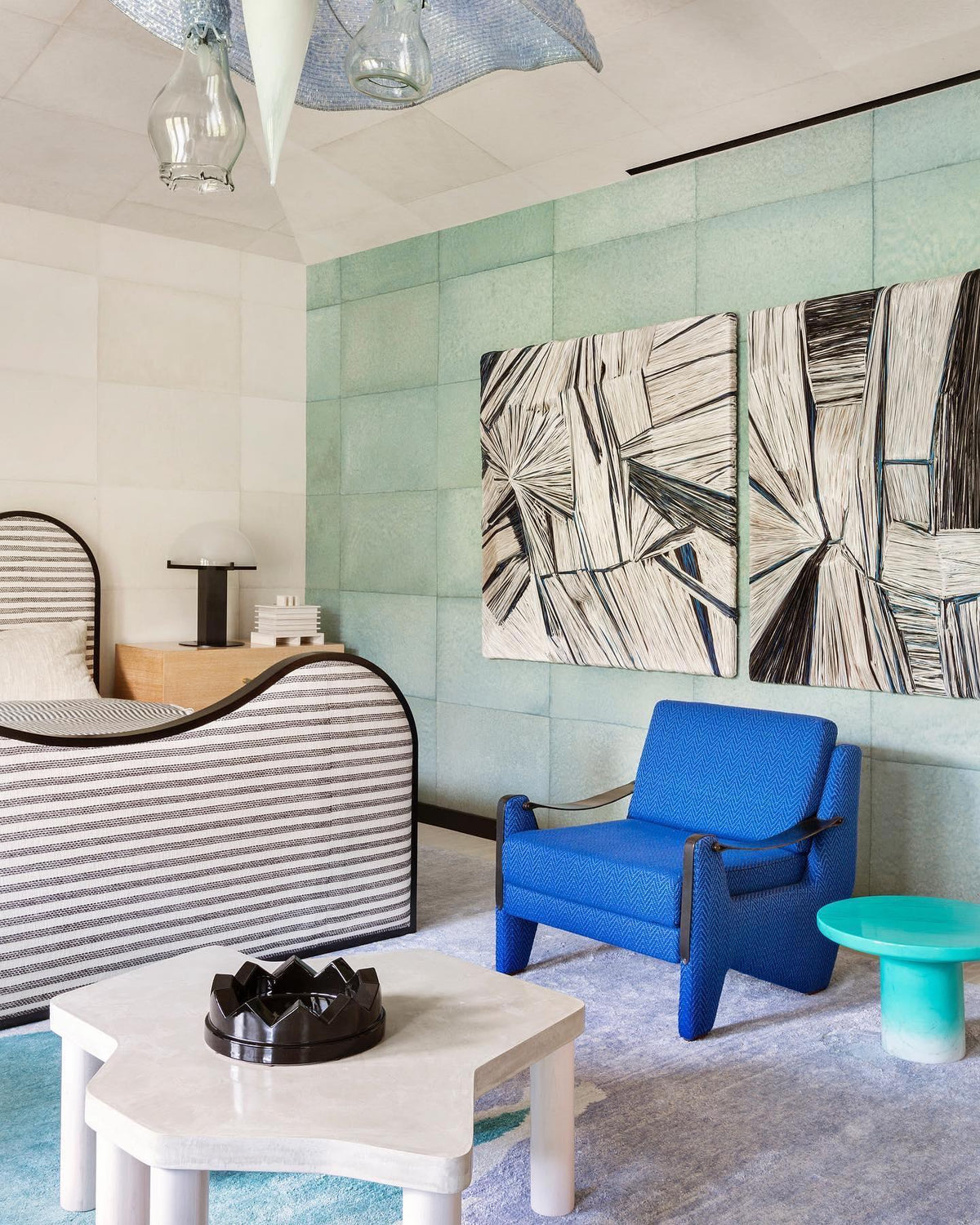Small Clérachic table lamp on a low shelf in a mint-green room, with striped furniture, a blue armchair and large graphic artwork.