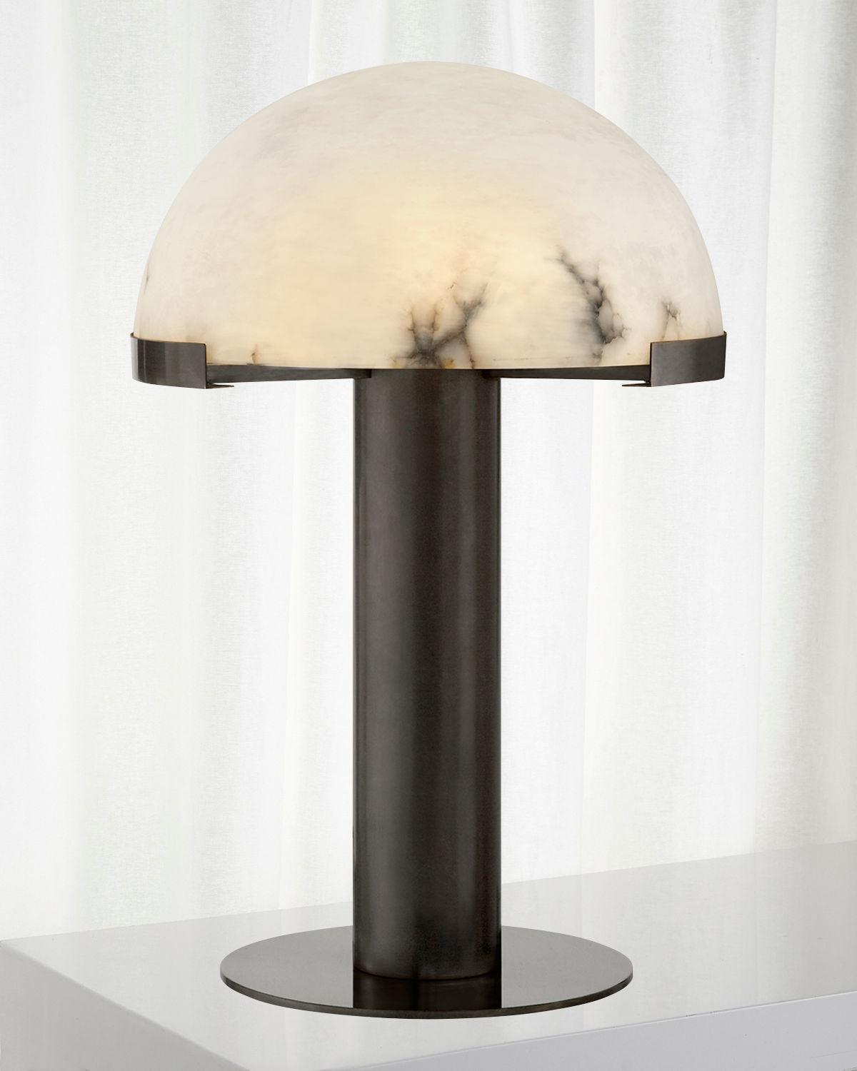 Dark bronze-coloured Clérachic table lamp with a black-veined alabaster dome, on a white surface in front of a pale curtain.