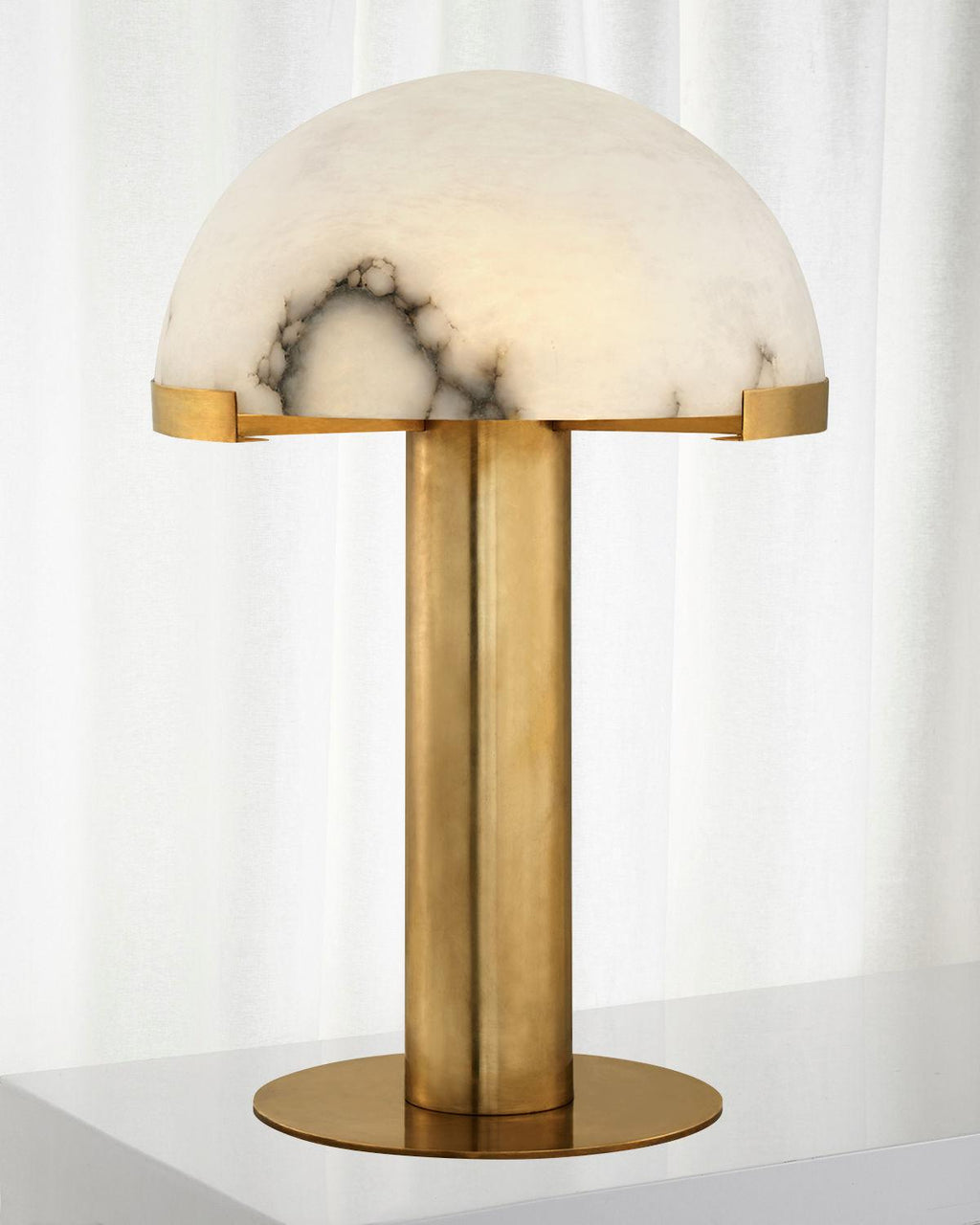 Gold Clérachic table lamp with a cloud-veined alabaster dome, standing in front of a sheer white curtain.