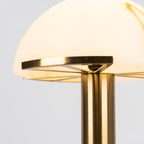 Close view of the brass rim and underside of the lit dome on this gold Clérachic table lamp, with the stem rising below.