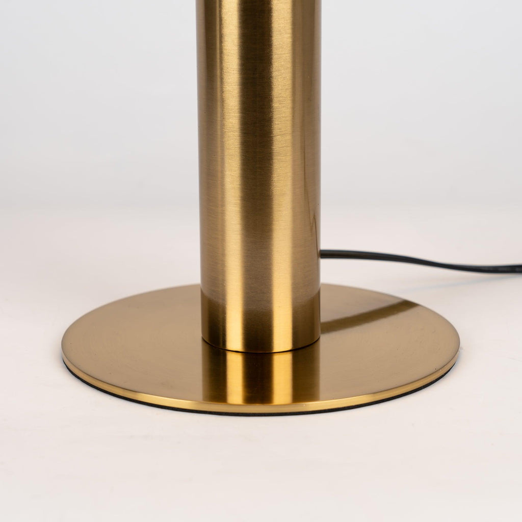 Close view of the brushed brass stem and round base of this Clérachic table lamp, with the black cord leaving at the back.