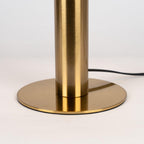 Close view of the brushed brass stem and round base of this Clérachic table lamp, with the black cord leaving at the back.