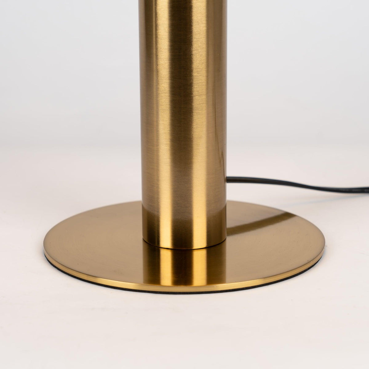 Close view of the brushed brass stem and round base of this Clérachic table lamp, with the black cord leaving at the back.
