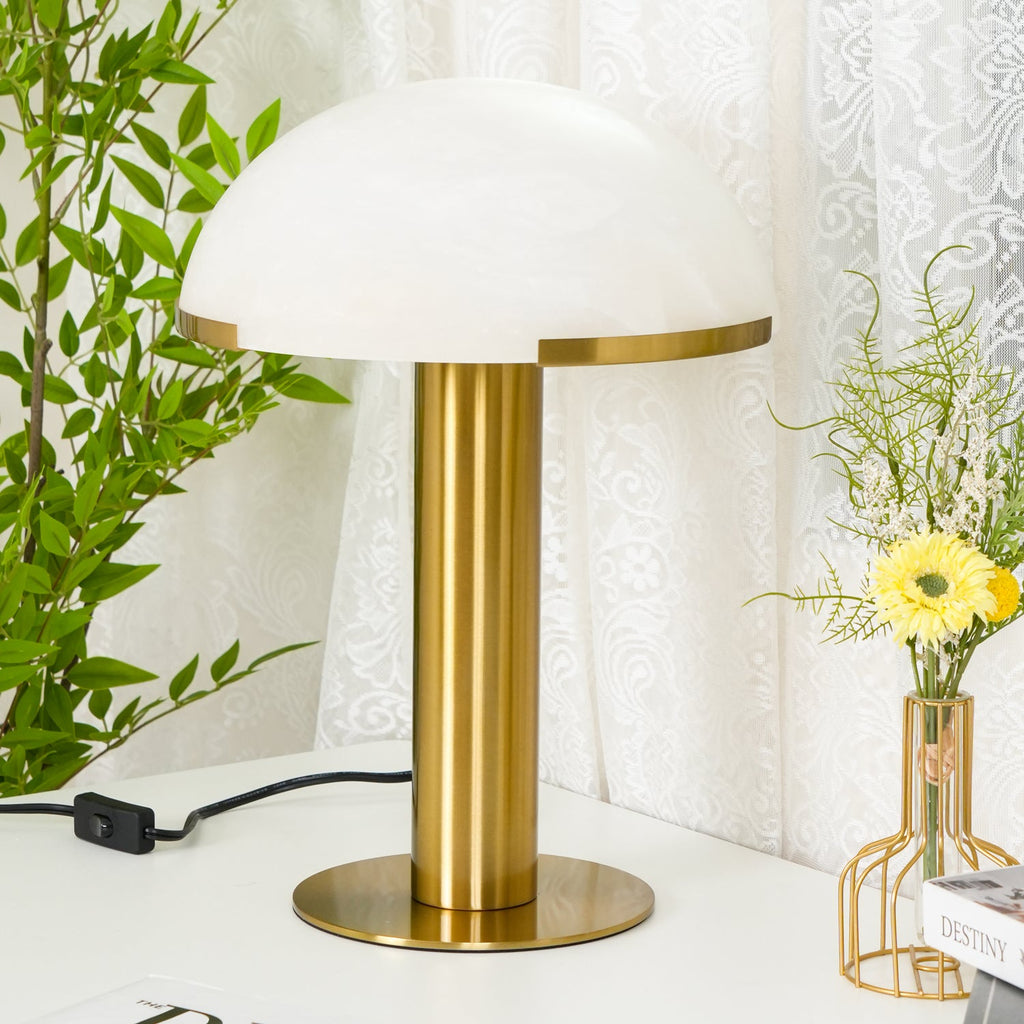 Larger view of this Clérachic table lamp in gold, with a white dome and a wide brass base next to a bunch of yellow flowers.