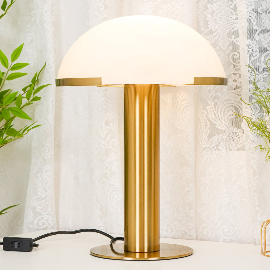 Lit gold Clérachic table lamp with a glowing white dome, filling most of the frame in front of a white lace curtain.