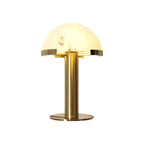 Gold Clérachic table lamp lit from within on a plain white background, the brass base ring catching the light.