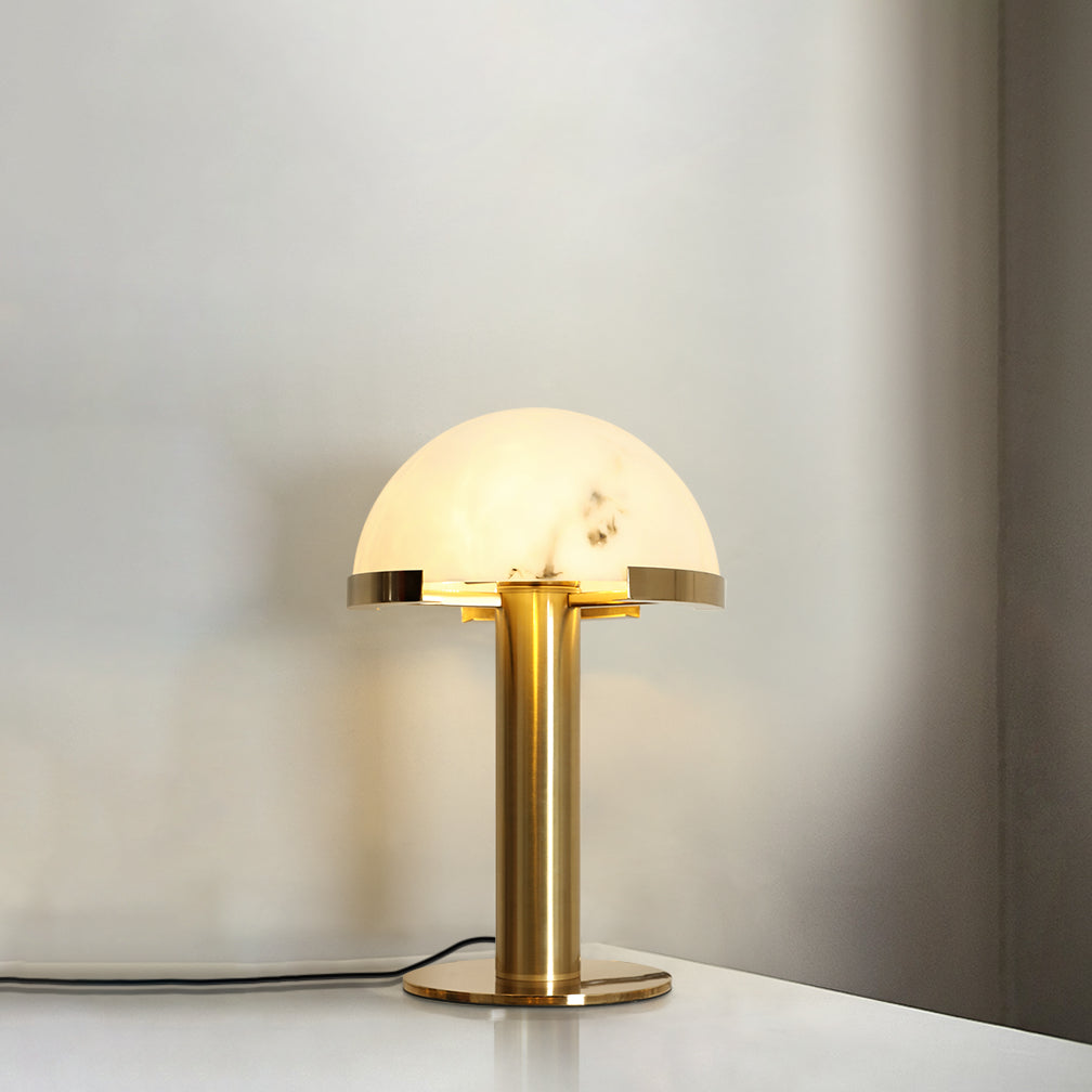 Gold Clérachic table lamp glowing on a light surface in a soft cream room, with the cord trailing across to the right.
