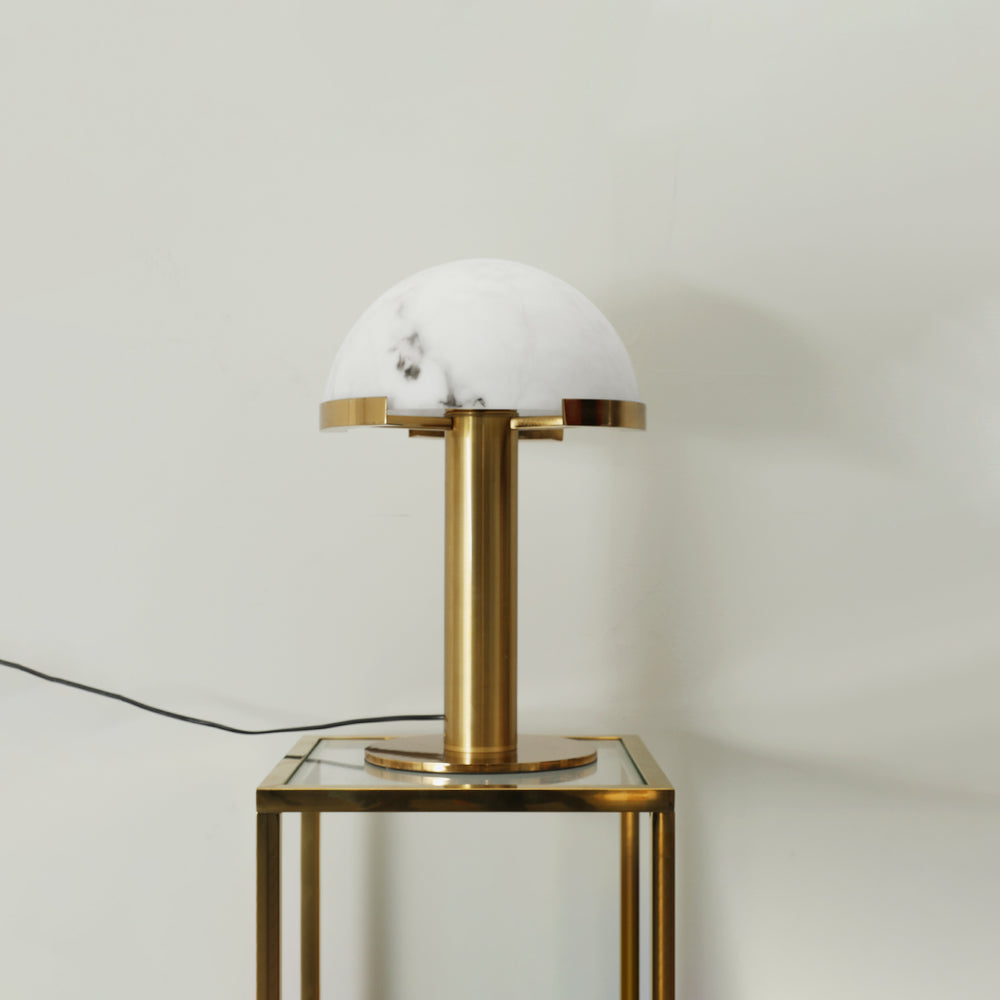 Gold Clérachic table lamp, unlit, on a glass-topped table with a gold frame, its cord running out to the left.