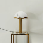 Gold Clérachic table lamp, unlit, on a glass-topped table with a gold frame, its cord running out to the left.