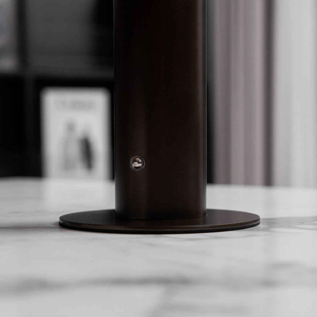 Close view of the dark bronze stem and round base of this Clérachic table lamp, with a small round fitting on the stem and a marble top.