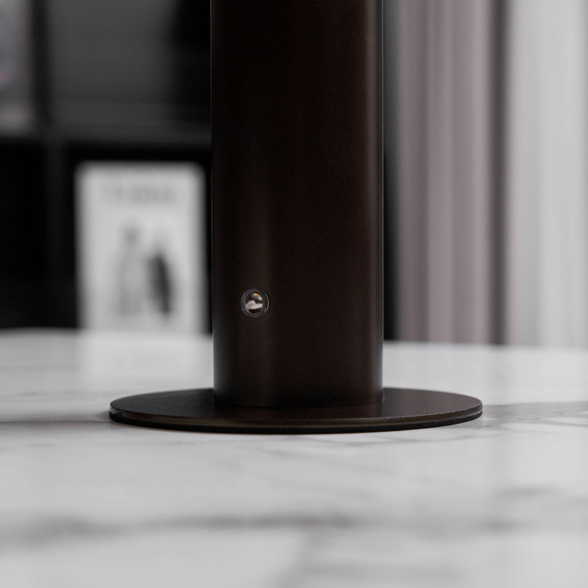 Close view of the dark bronze stem and round base of this Clérachic table lamp, with a small round fitting on the stem and a marble top.
