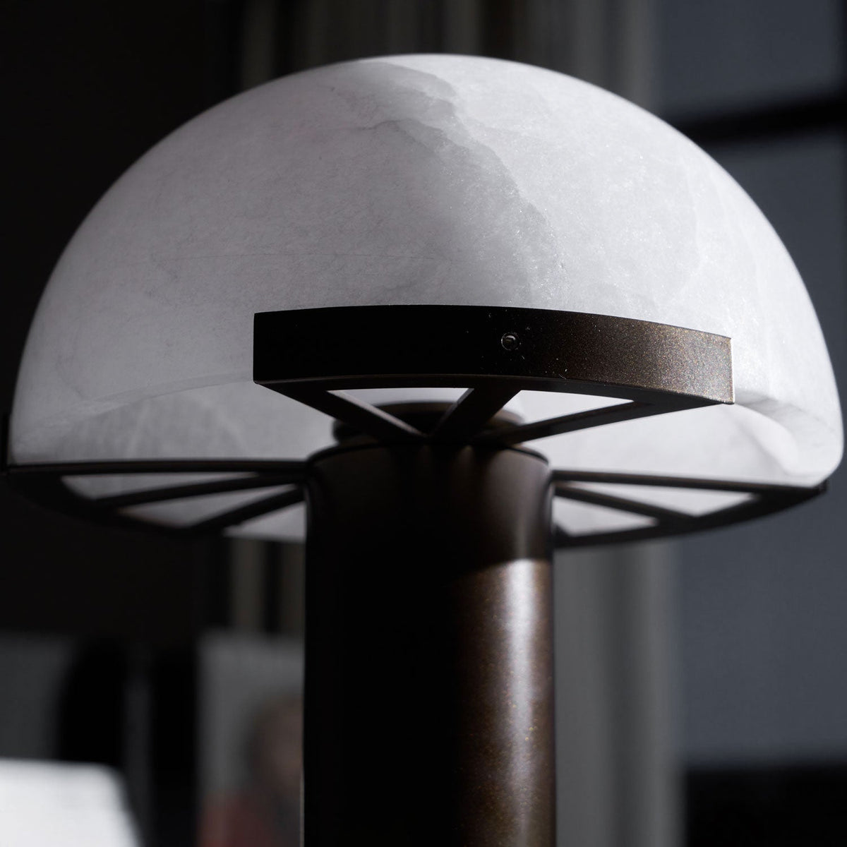 Close view of the frosted white dome and dark bronze ring of this Clérachic table lamp, with the stem blurred in front.