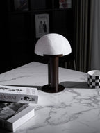 Dark bronze-coloured Clérachic table lamp on a white marble table, seen from a higher angle with books and a mug at the edges.