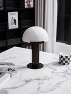 Dark bronze-coloured Clérachic table lamp at a low angle on a marble top, with a chequered mug and a stack of books beside it.