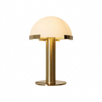Gold Clérachic table lamp lit from within, with a brass stem and round base on a plain white background.