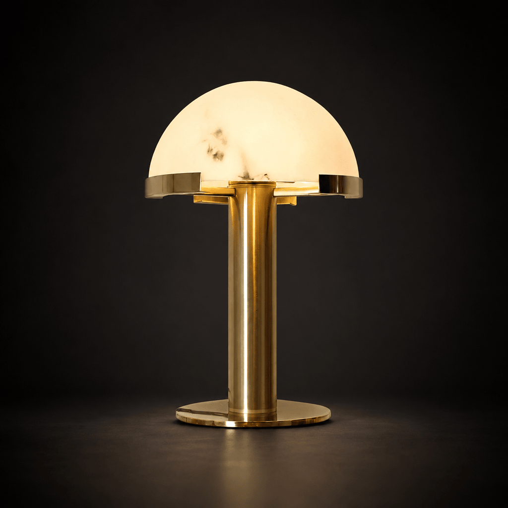 Gold Clérachic table lamp lit against a dark charcoal backdrop, the veined dome glowing and the brass base reflecting the light.
