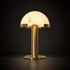 Gold Clérachic table lamp lit against a dark charcoal backdrop, the veined dome glowing and the brass base reflecting the light.