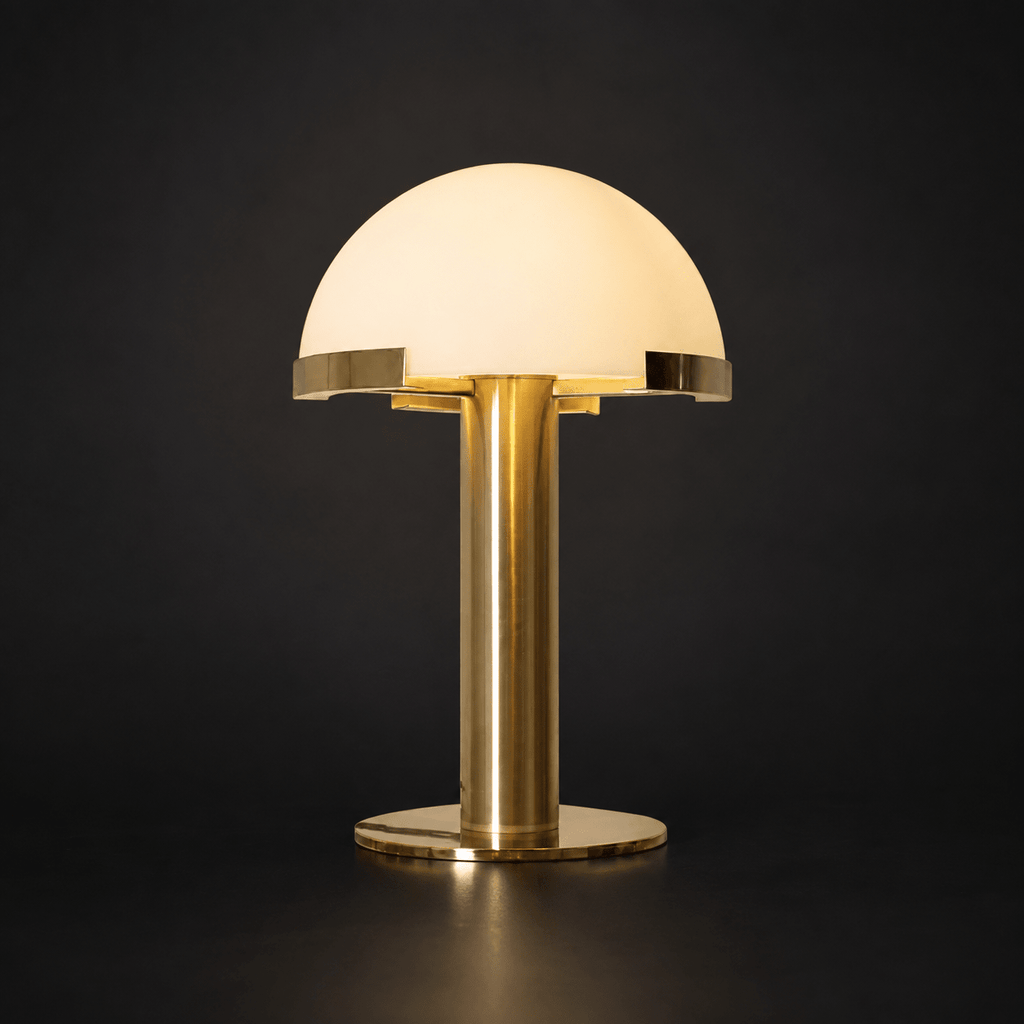 Gold Clérachic table lamp on a dark backdrop, with a smooth glowing white dome and a polished brass base.
