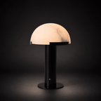 Black Clérachic table lamp lit in the dark, the dome glowing pink-white with fine grey veins above a round black base.