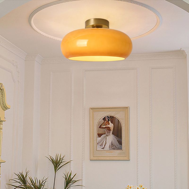 The Clérachic Puffed Oval Glass Ceiling Light in orange glass, flush against a moulded ceiling rose above panelled walls.