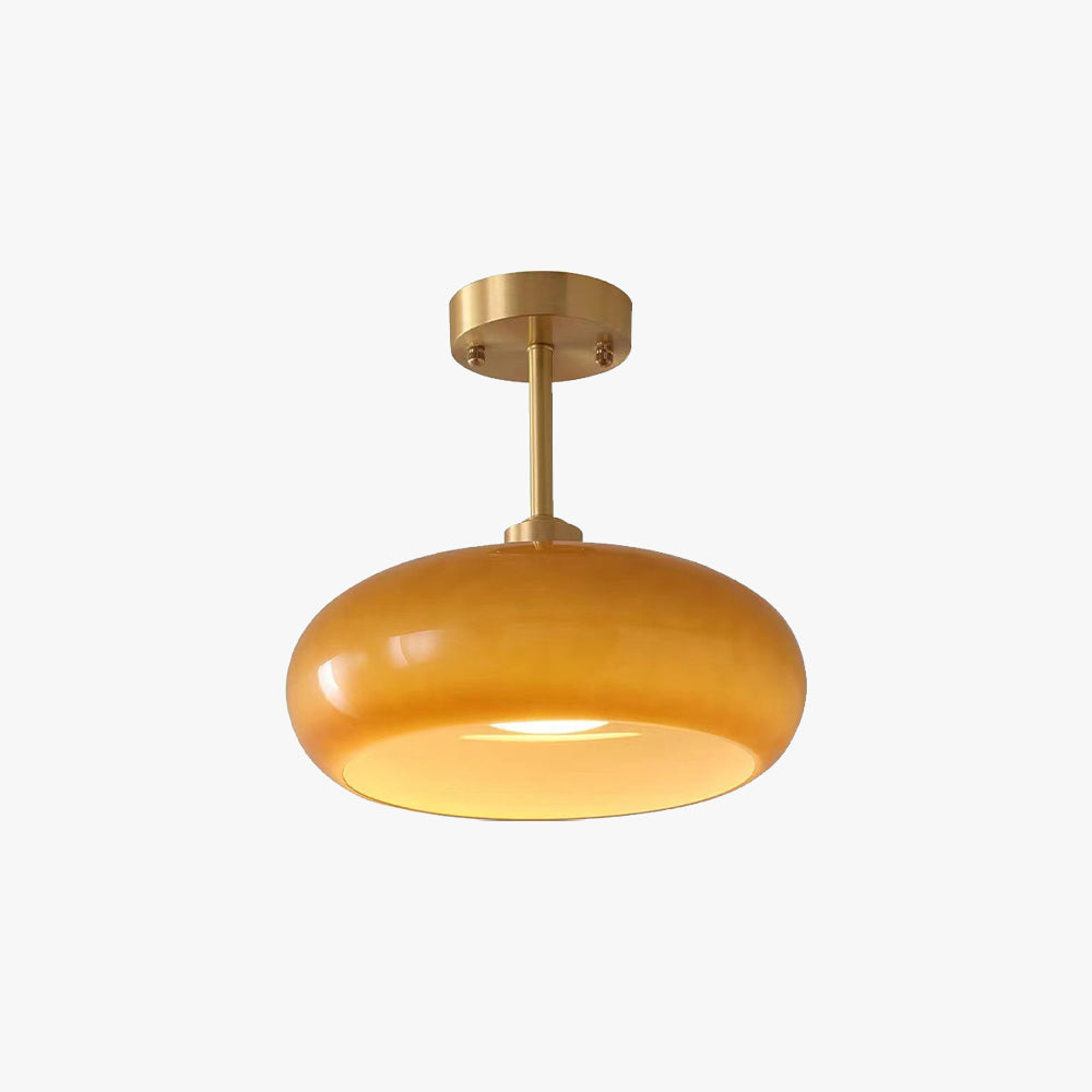 Studio view of the Clérachic Puffed Oval Glass Ceiling Light in orange glass, lit on its short brushed brass drop rod.