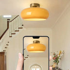 A phone camera framing the orange Clérachic Puffed Oval Glass Ceiling Light lit above a staircase landing.