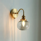 Clérachic Pull-Chain Brass Wall Sconce in smoke gray glass, the smooth squat globe warming the light against a soft grey-blue wall.