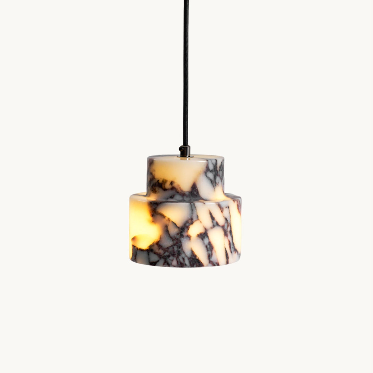 Two-tier Clérachic pendant in purple-veined white marble on a black cord, glowing amber, on a plain off-white backdrop.