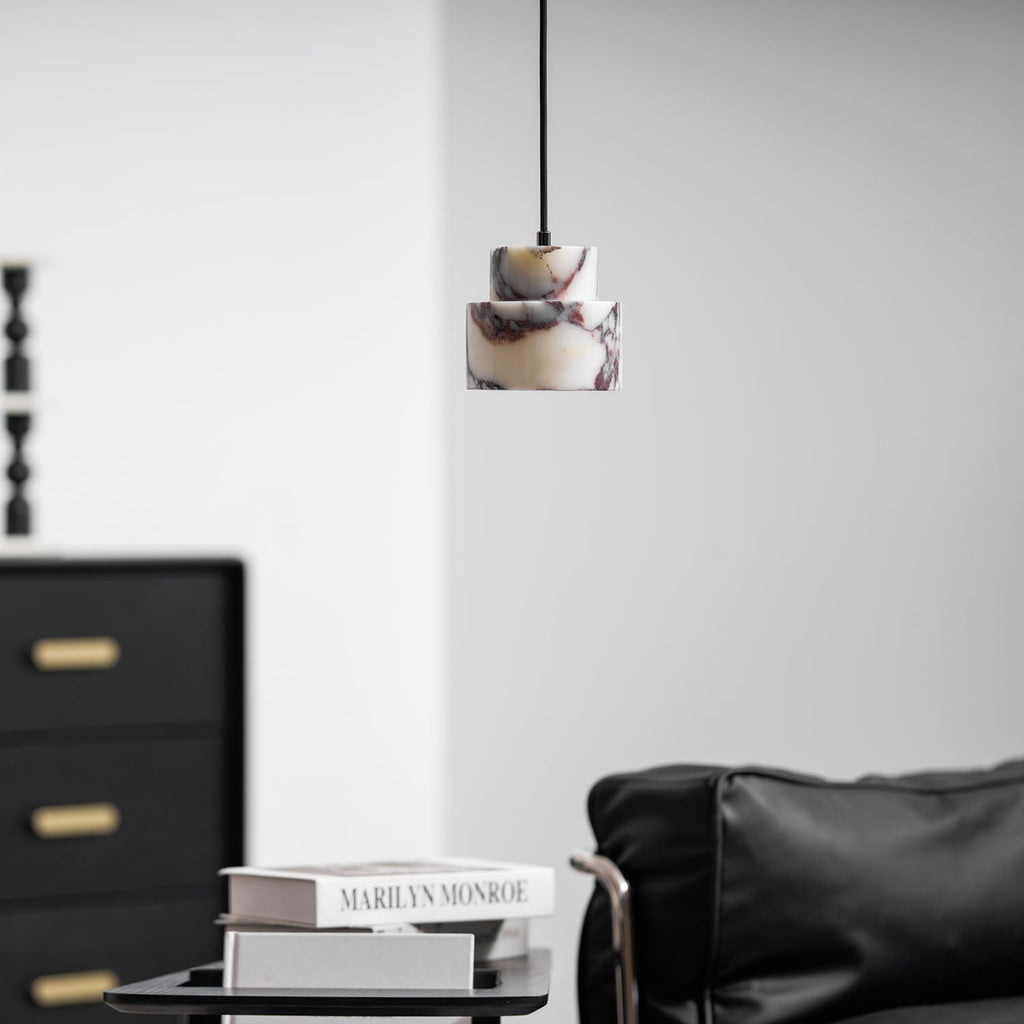 A small marble Clérachic pendant hangs high in a bright room, above a stack of books and a black leather armchair.